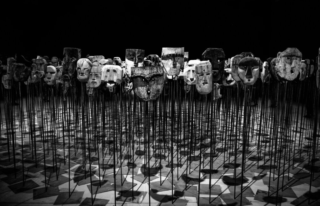 pexels-photo-669319-669319 An artistic display of wooden masks on poles, set in a dimly lit theater.